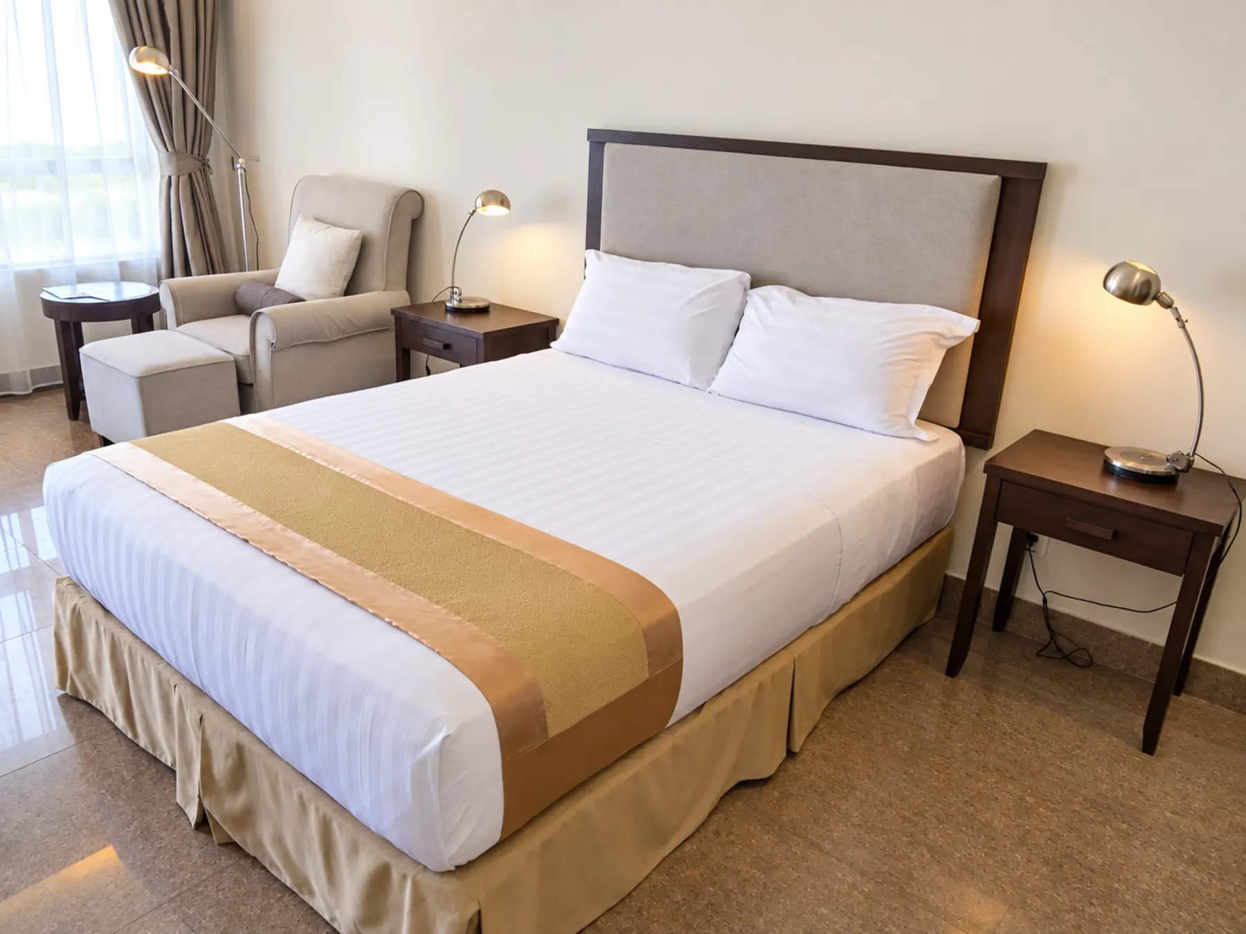 Quarto Deluxe — cama queen com faixa dourada, candeeiros de cabeceira e poltrona
