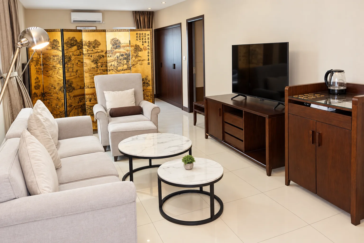 Suite Deluxe — sala de estar com sofá, poltrona, biombo dourado e televisão